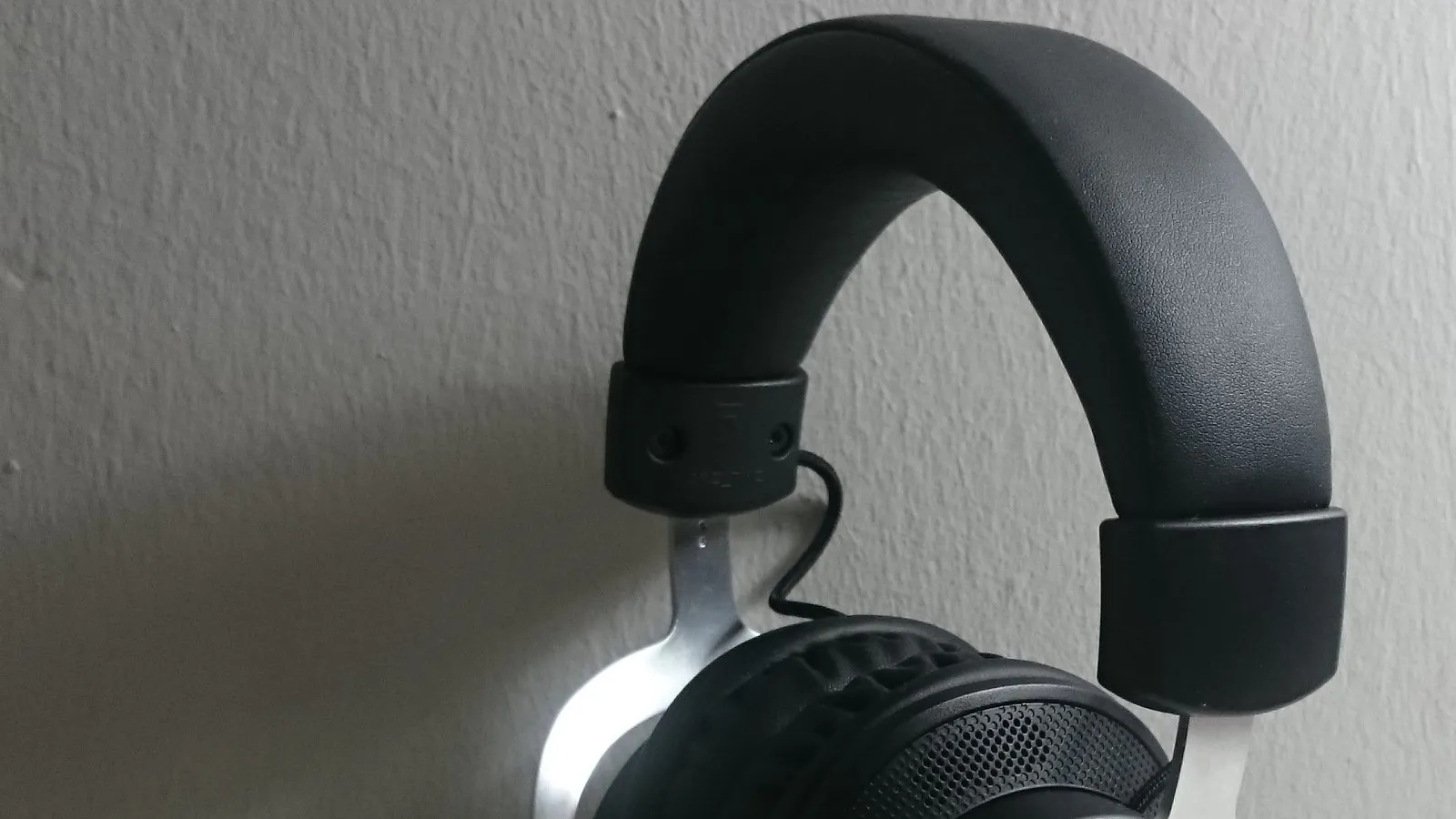 Detalhe da armação e da concha acolchoada de um headset gamer com fio, mostrando o reforço metálico e o material da almofada.