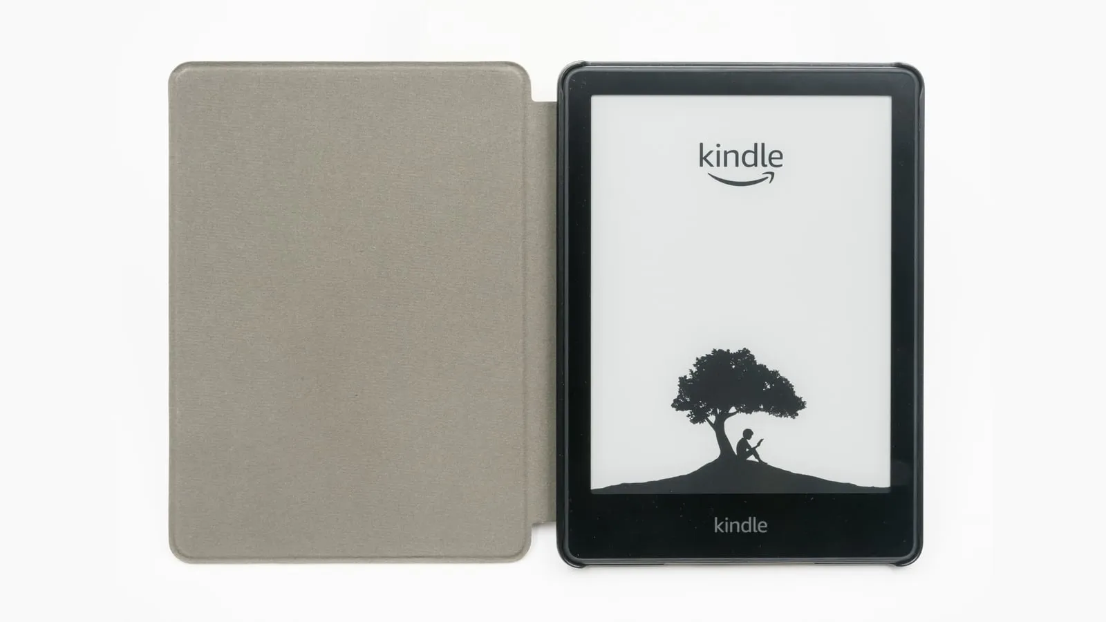 Kindle Paperwhite com a capa aberta ao lado, mostrando na tela o logotipo do Kindle e a ilustração de uma pessoa lendo sob uma árvore.