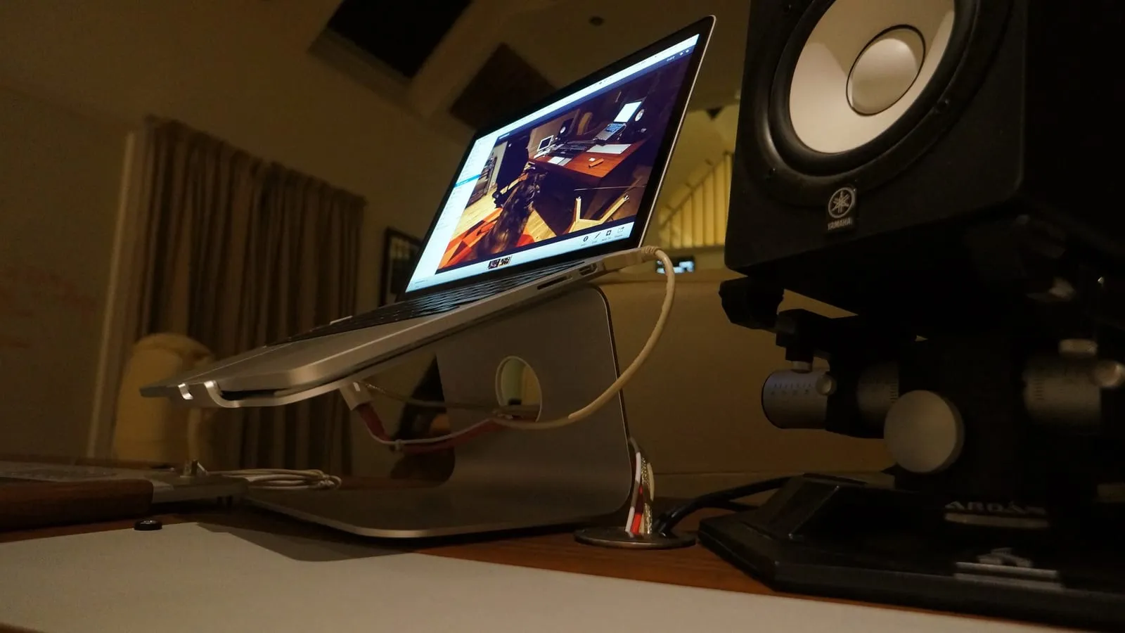 Notebook elevado sobre um suporte de alumínio numa mesa, ao lado de um monitor de áudio.