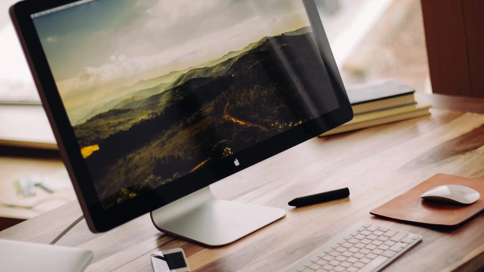 Monitor sobre mesa de madeira com teclado, mouse e caderno em uma escrivaninha de home office.