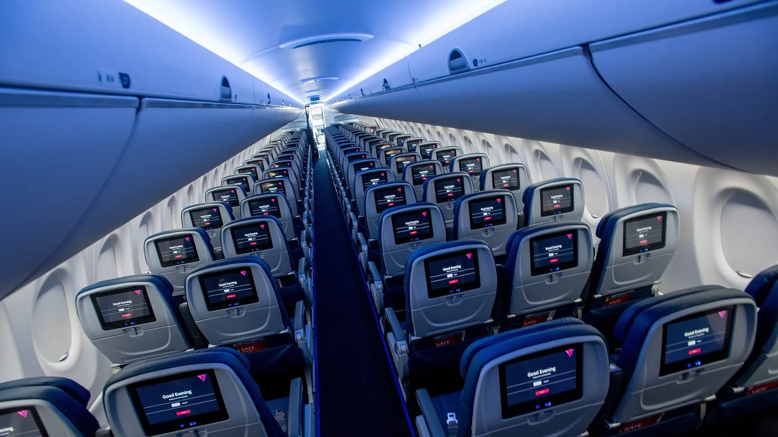 Corredor de uma cabine de avião vazia, com as telas dos assentos ligadas.